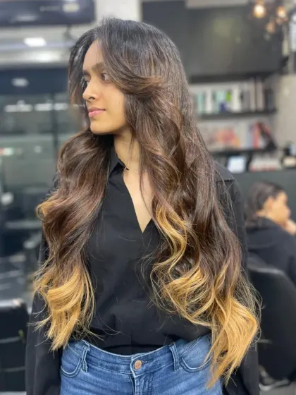 A dramatic and beautiful ombre effect on very long hair, transitioning from a dark root to bright blonde ends, styled in soft waves.