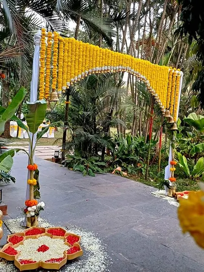 A traditional marigold archway at the entrance, complete with hanging bells and a floral rangoli.