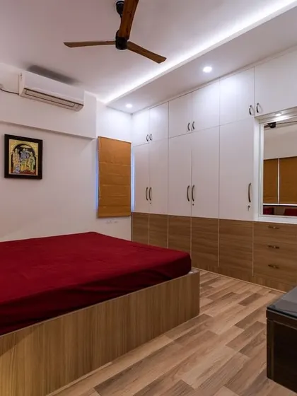 This bedroom maximizes storage with floor-to-ceiling white wardrobes, contrasted with a bold red bedspread and warm wood flooring and paneling.