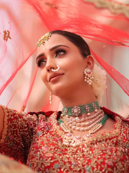 Presenting Ishq. A bride framed by her red veil, her pearl and emerald jewelry adding a touch of softness to the look.