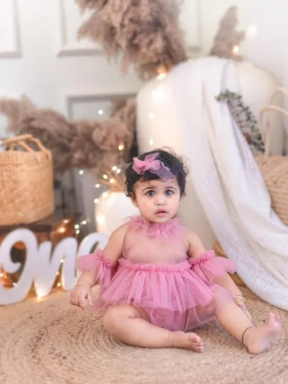 A sweet portrait of a one-year-old girl sitting up in her birthday setup. Her curious expression is perfectly captured in this milestone photo.