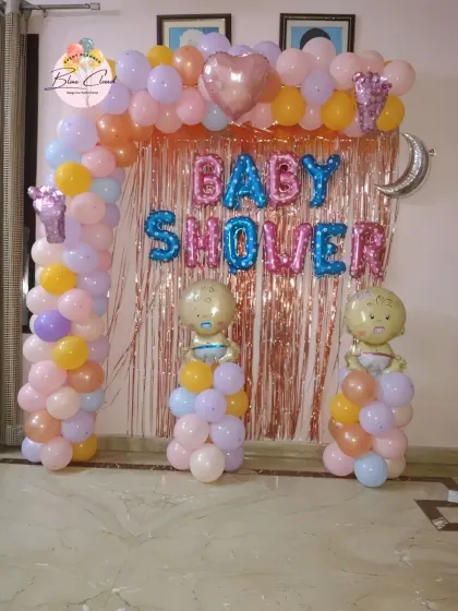 A pastel-colored baby shower decoration with a balloon arch, shimmer curtain, and baby-themed foil balloons.
