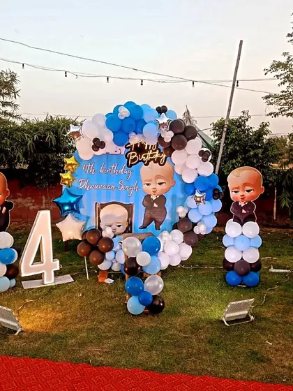 An outdoor Boss Baby theme for a 4th birthday, featuring a balloon arch and character cutouts on a green lawn.