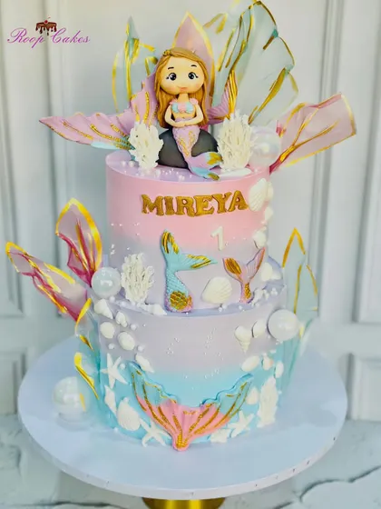 A magical two-tier mermaid theme cake with iridescent fins, seashells, and a beautiful fondant mermaid.
