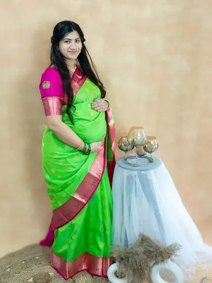 A lovely studio portrait of a mom-to-be in a traditional green and pink saree.