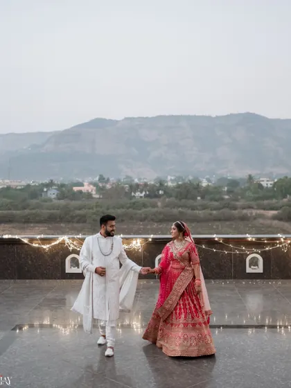 A stunning wide shot of the couple walking hand-in-hand on a terrace with a mountain range in the background.
