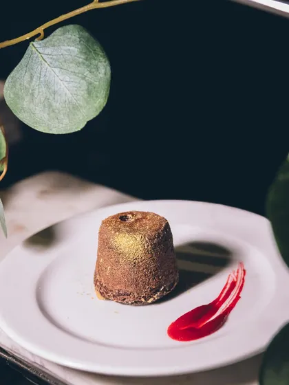 A rich chocolate lava cake, dusted with gold and served with a raspberry coulis.