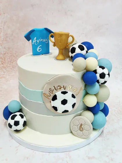 We score a goal with this stylish football champion cake. A personalized jersey, a golden trophy, and a cascade of footballs and spheres in team colors adorn this modern cake, making it the perfect centerpiece for a football fan's birthday.