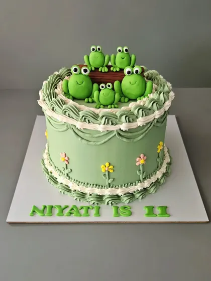 A fun froggy family cake for Niyati's 11th birthday. This Lambeth-style cake combines vintage piping with cute, hand-sculpted green frogs for a unique and whimsical design.