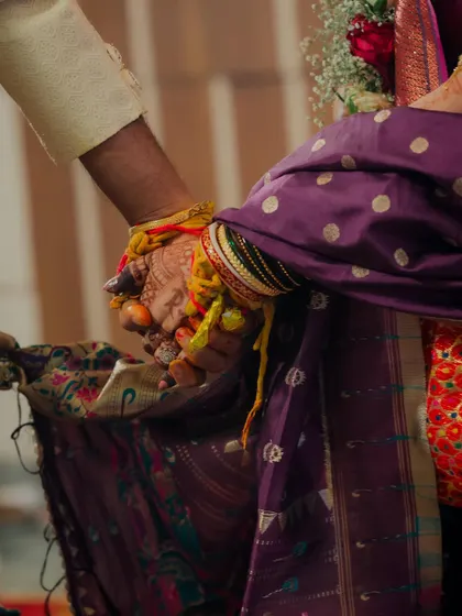 A close-up shot of the couple holding hands during the ceremony. This image focuses on the connected hands, adorned with turmeric and sacred threads, symbolizing their union and shared path forward.