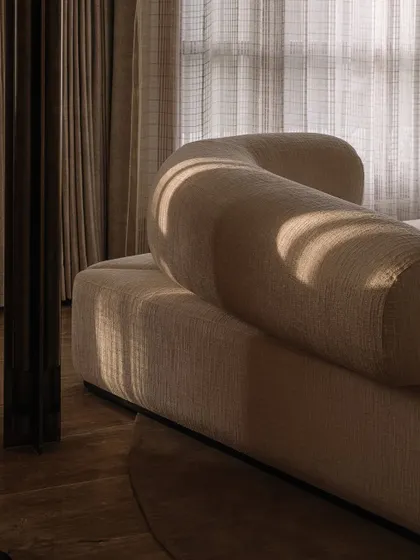 The play of light and shadow on the curved, upholstered forms of this custom sofa highlights its sculptural quality. We focus on creating furniture with soft, inviting silhouettes that anchor a room.