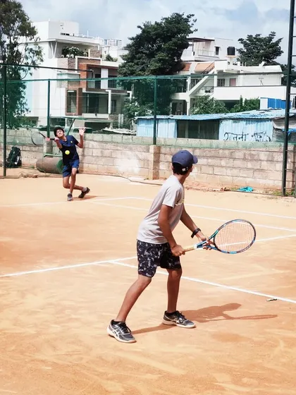 A doubles match in progress at the AITA U-14 tournament, with players positioned for a competitive rally.