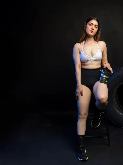 A full-length shot of a female model posing with a supplement bottle, using negative space to draw focus to her and the product.