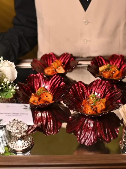 A server presents a tray of Asian-style cottage cheese appetizers in vibrant red flower-shaped bowls.