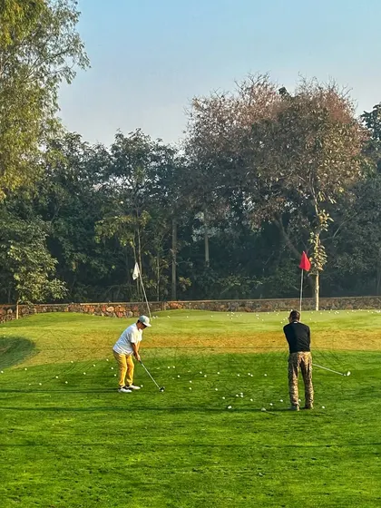 Golfers practice on the putting green under a beautiful sky, locked in on their game.