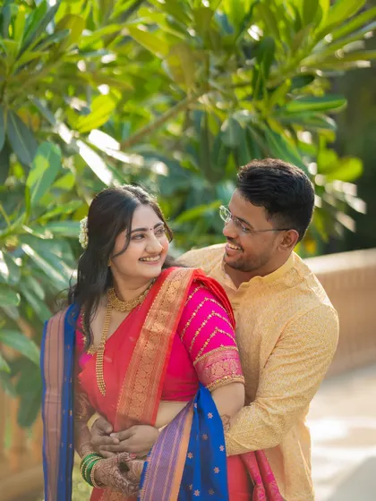 A candid and joyful moment between Jagruti and Shubham. The natural, leafy background complements their vibrant traditional outfits.