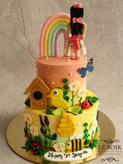 This two-tier garden theme cake for Sayuri's 5th birthday is full of whimsical details. The 1.5 kg Chocolate Butterscotch cake features a fondant figurine, a birdhouse, bees, and buttercream flowers.