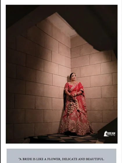 A solitary, artistic shot of bride Ahana in her red lehenga, standing against a stone wall with dramatic lighting.