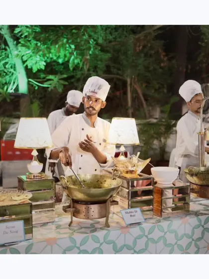A chef at a live counter preparing a traditional Indian curry in a brass kadai, surrounded by fresh ingredients and elegant serveware.
