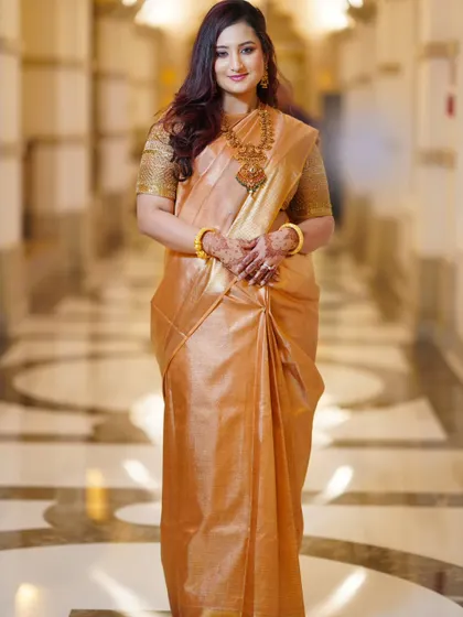 A full-length portrait showcasing the bride's graceful posture and the beautiful drape of her golden silk saree. She exudes confidence and elegance.