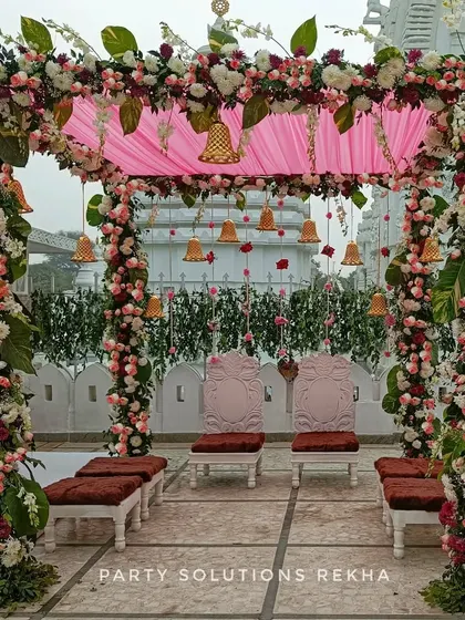 A beautiful mandap setup at a temple. The structure is heavily decorated with pink and white flowers, with hanging temple bells adding a traditional and auspicious element to the sacred ceremony.