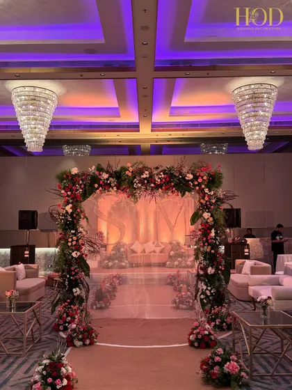 A floral archway is a timeless symbol of new beginnings. For this engagement, I created a lush arch filled with red and pink flowers, framing a sheer curtain with the couple's initials for a personalized and romantic entrance to the stage area.