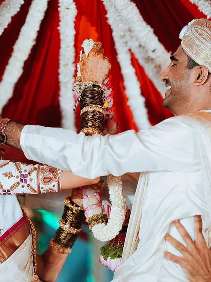 The groom joyfully helps the bride with her garland during the ceremony, a sweet and candid interaction.