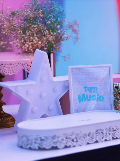 A light-up star and a "Turn up the Music" sign create a cool, ambient glow on the dessert table, highlighting the pastel and musical theme of the party.