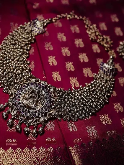A stunning piece of bridal jewelry, a silver-toned choker with a large pendant, laid out on a rich red silk background. This shot highlights the beauty and craftsmanship of the accessory.