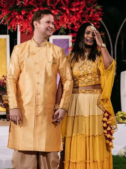 A happy couple at their colorful pre-wedding event. The yellow and red floral decor creates a bright and festive atmosphere perfect for celebrating.