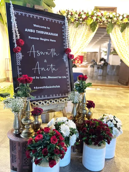 A beautiful welcome board for a Tamil wedding, featuring red roses and traditional brass vases.