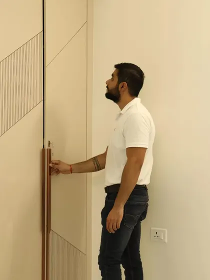 A close-up of a wardrobe door with a unique design. The combination of plain laminate with a diagonally grooved panel and a long copper-finish handle creates a stylish, custom look.