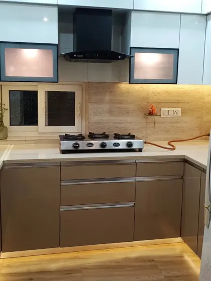 This L-shaped modular kitchen features beige upper cabinets and brown lower cabinets, complemented by wooden flooring.