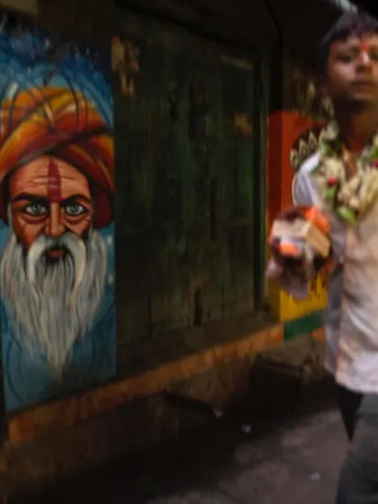 A man walks with a slight motion blur through a lane, past a painted mural of a sadhu. This shot captures the constant movement of life in Varanasi, where the spiritual and the everyday flow past each other.