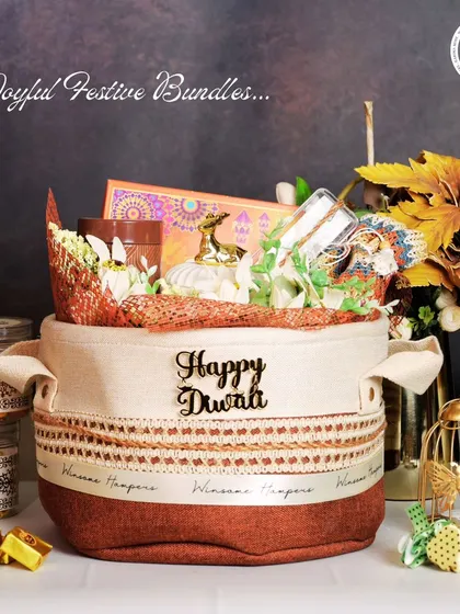 A cozy and rustic "Happy Diwali" hamper in a fabric-lined basket. This gift set includes jars of gourmet treats, a miniature deer figurine, and other festive decor, creating a warm and inviting present for the festival of lights.