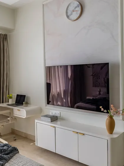 The functional side of the sage green master bedroom, featuring a sleek white workspace and a TV mounted on a wall with custom wallpaper and molding.