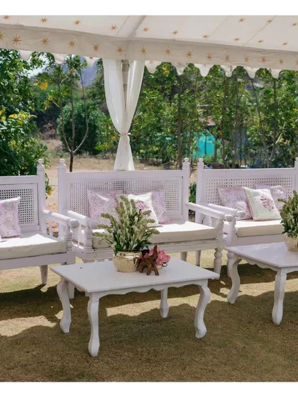 A lovely outdoor seating arrangement for a Bhaat and Mehendi ceremony, featuring white wooden furniture and delicate floral-printed cushions.
