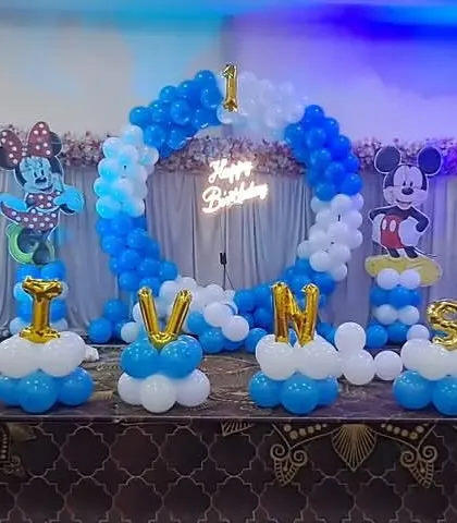 A Mickey Mouse and Boss Baby themed birthday party. The decor includes a circular balloon arch, character cutouts, and balloon letters spelling out the child's name, 'SHIV'.