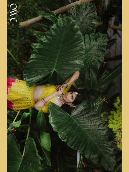 An aerial shot of the bride lying amongst giant leaves, a truly unique and artistic take on Haldi portraits.