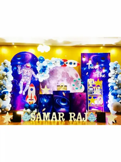 A full-stage space theme for Samar Raj's second birthday. This expansive setup includes multiple galaxy backdrops, an astronaut cutout, and rocket ships for a complete interstellar experience.