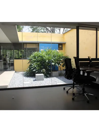 An office interior at Karunashraya, with a floor-to-ceiling glass wall looking into a private gravel court.