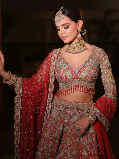 The delicate tassels on the blouse and the scalloped edge of the dupatta add a touch of modern design to this traditional red lehenga.