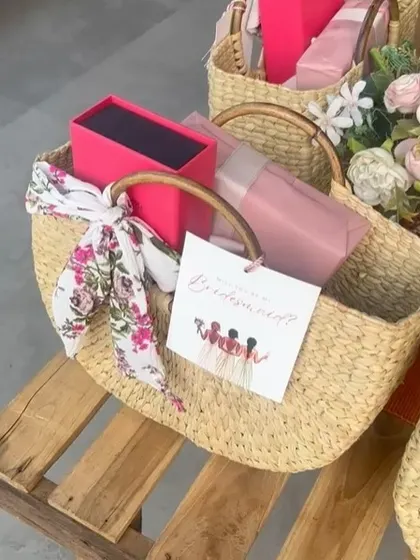 A bridesmaid proposal basket, complete with a "Will you be my bridesmaid?" card. The handwoven basket is filled with pink-themed gifts and tied with a floral scarf.