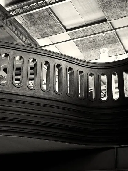 A perspective that showcases the undulating form of the mezzanine railing against the industrial ceiling structure.