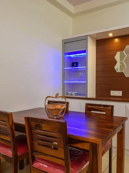 A dining area with a custom crockery unit. The unit features a bar section with blue ambient lighting, a solid wood dining table, and a decorative wall with hexagonal mirrors.