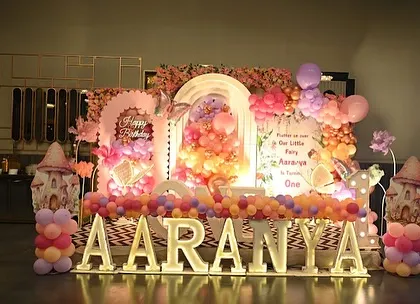A full stage view for Aaranya's butterfly party, showcasing the large marquee letters, a multi-layered backdrop with a floral ring, and whimsical mushroom props.
