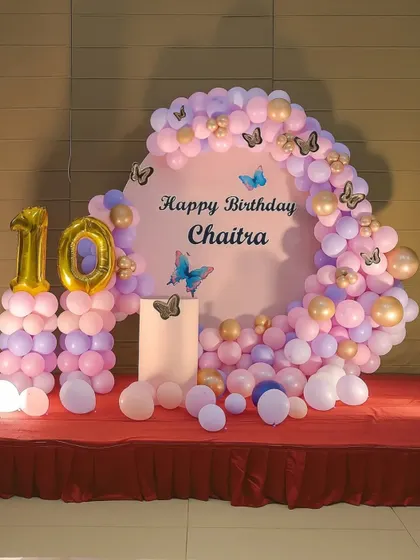 A butterfly-themed 10th birthday decoration. The setup features a circular backdrop, a pink and purple balloon arch with butterfly cutouts, and balloon pillars with the number '10'.