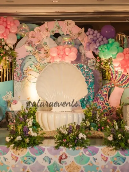 The main stage for Swara's mermaid-themed first birthday. The entire setup is a visual feast of pastel colors, shimmering details, and underwater motifs, centered around a beautiful seashell throne.