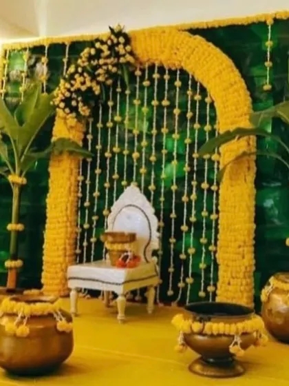 A traditional Haldi or pooja setup featuring a banana leaf backdrop, a marigold arch, and brass pots. This design is rooted in authentic customs and natural materials.