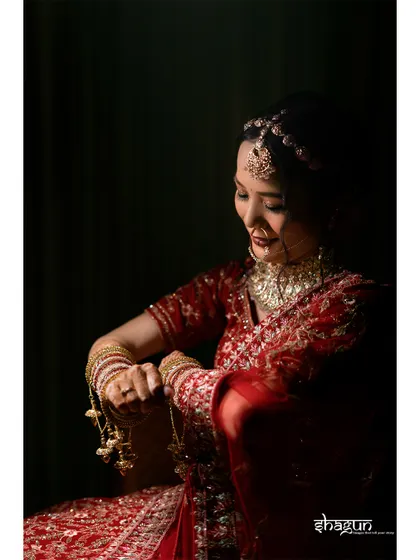 Grace personified. A low-light portrait of the bride, focusing on her traditional red attire and the intricate details of her kaleeras.